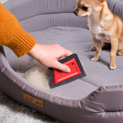 Hand using the red pet hair remover to gather loose fur from a fabric pet bed